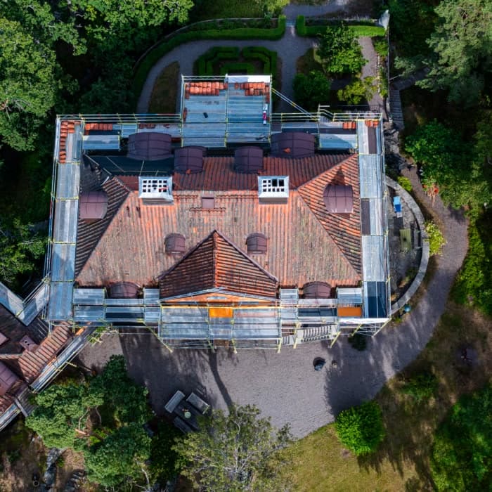 Villa med tegeltak och byggnadsställning runt taket, drönarbild
