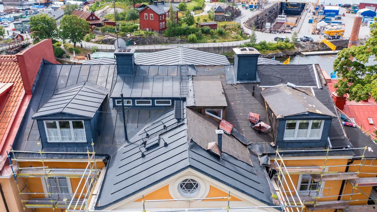 Gult hus med nytt plåttak och takkupor, byggnadsställning runt om